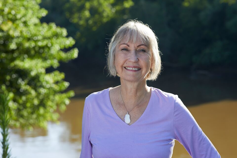 An older woman smiling in front of a river.