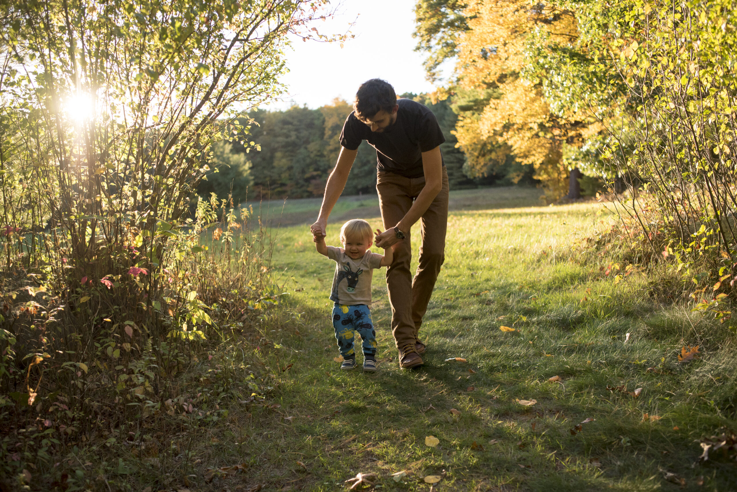 A man and a child walking down a path in the woods.