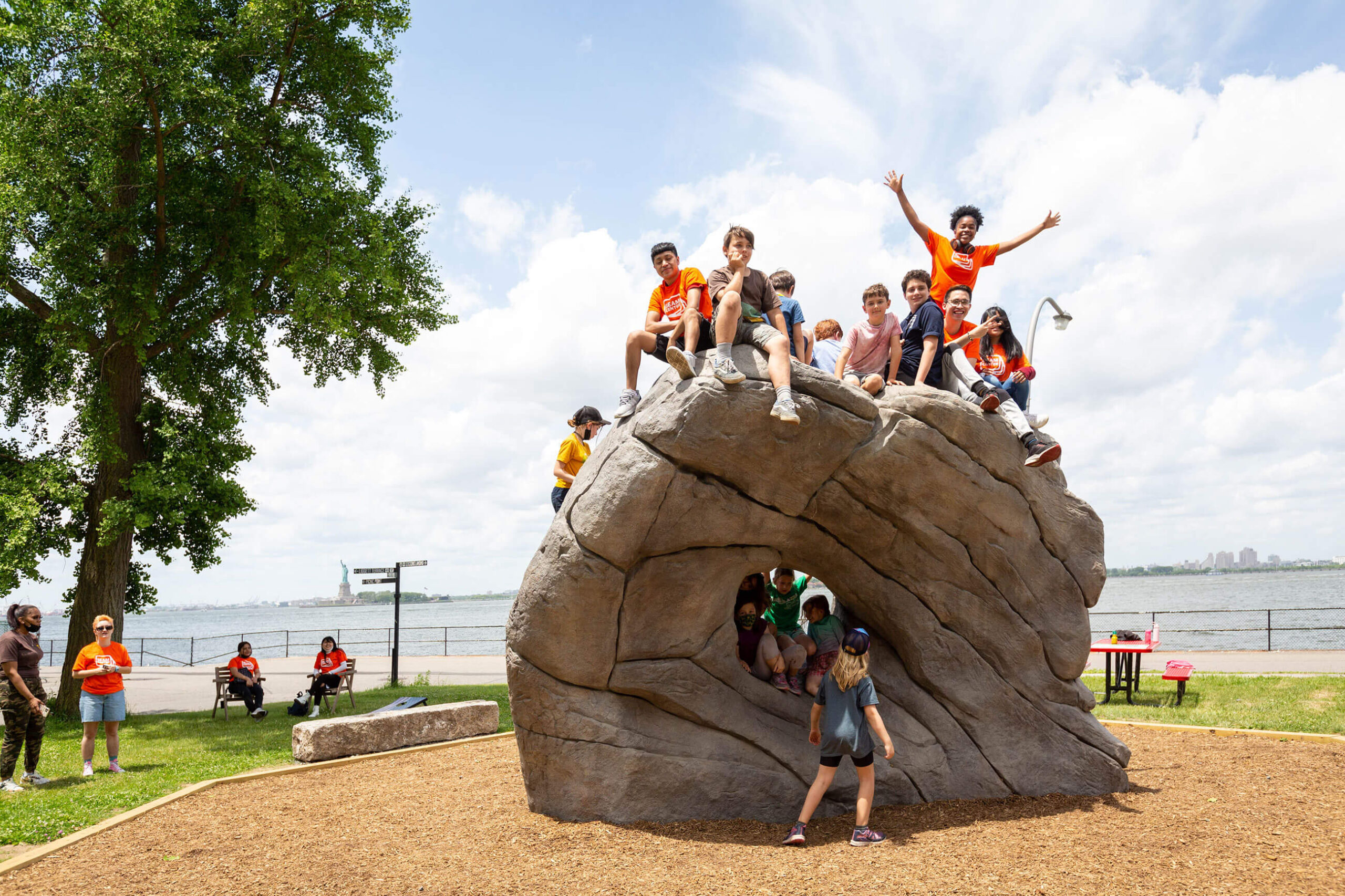 More than a dozen kids climbing and playing on a large donut-shaped rock and climbing structure at the Governors Island in New York.
