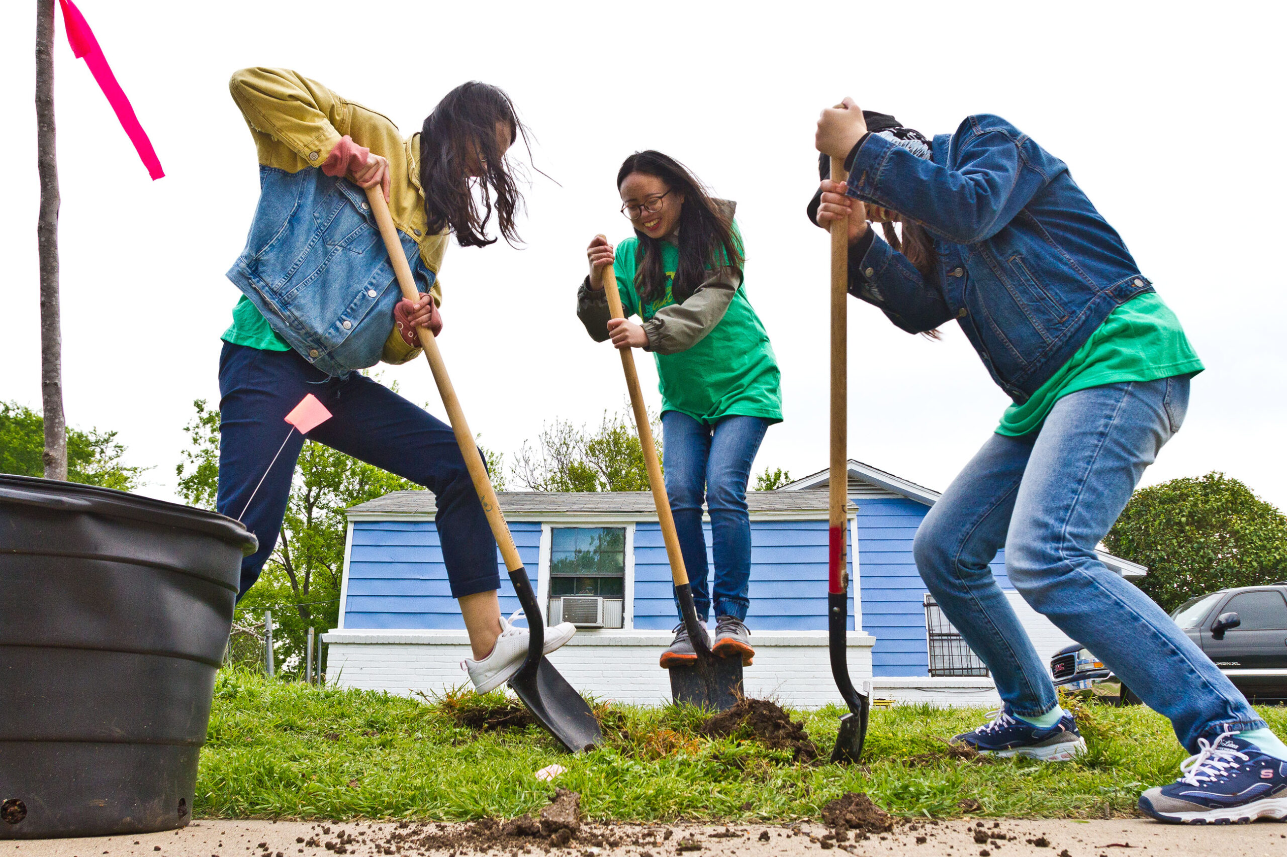 Three young people enthusiastically dig at a tree-planting event at a park in Dallas.