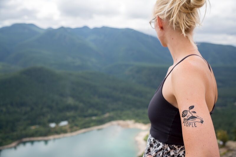 A woman with a tattoo on her back overlooking a lake.