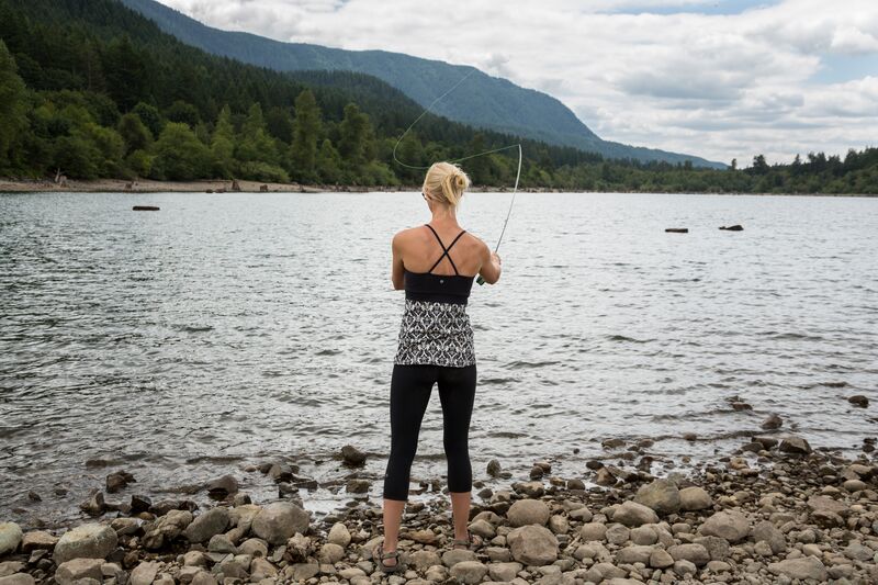 A woman is fishing in a lake with mountains in the background.