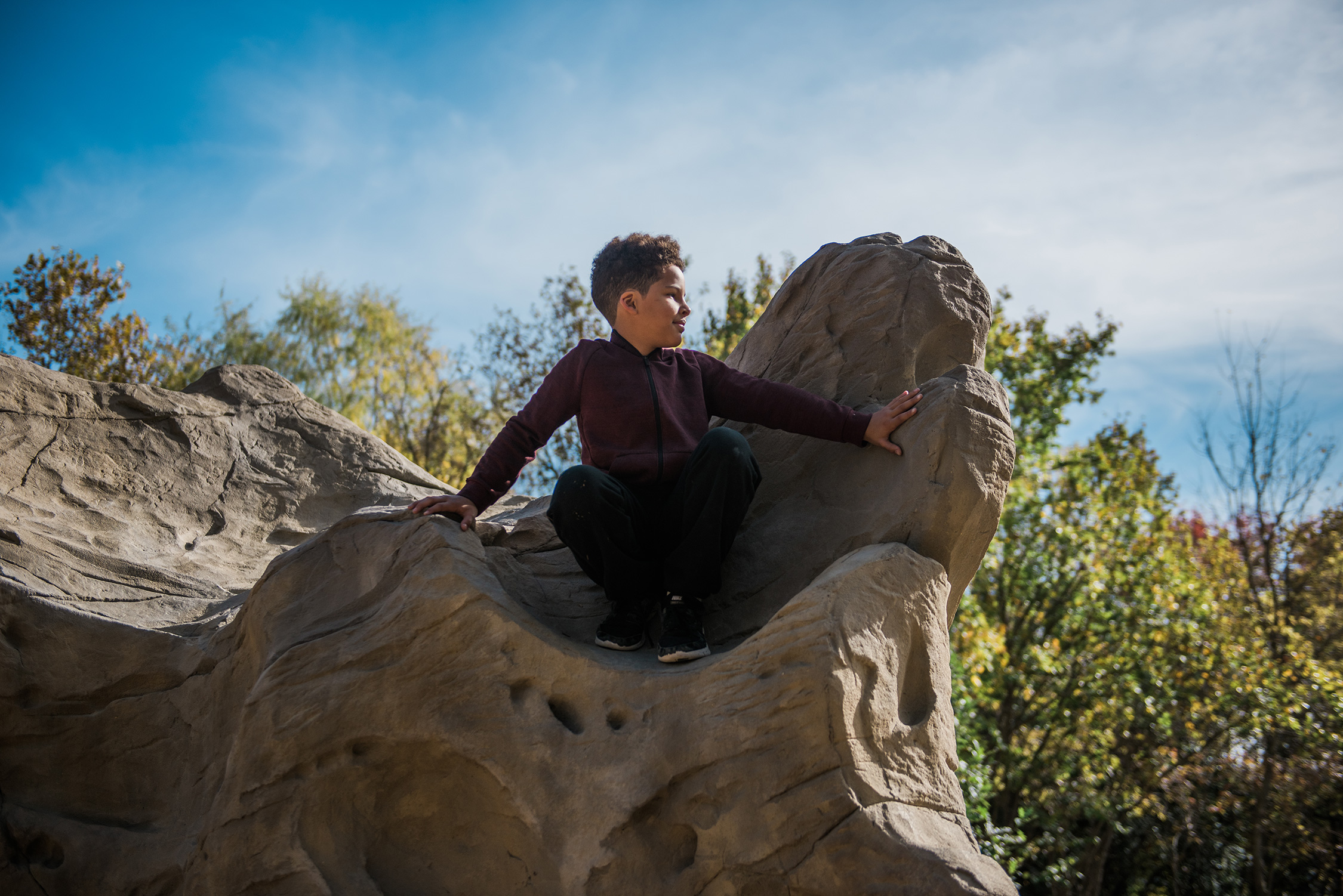 A boy sitting on a rock in a park.
