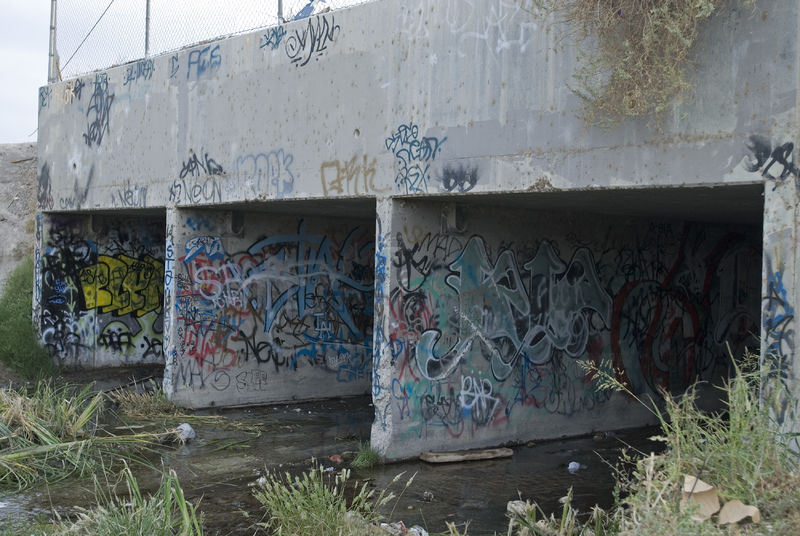 A graffiti covered bridge over a creek.