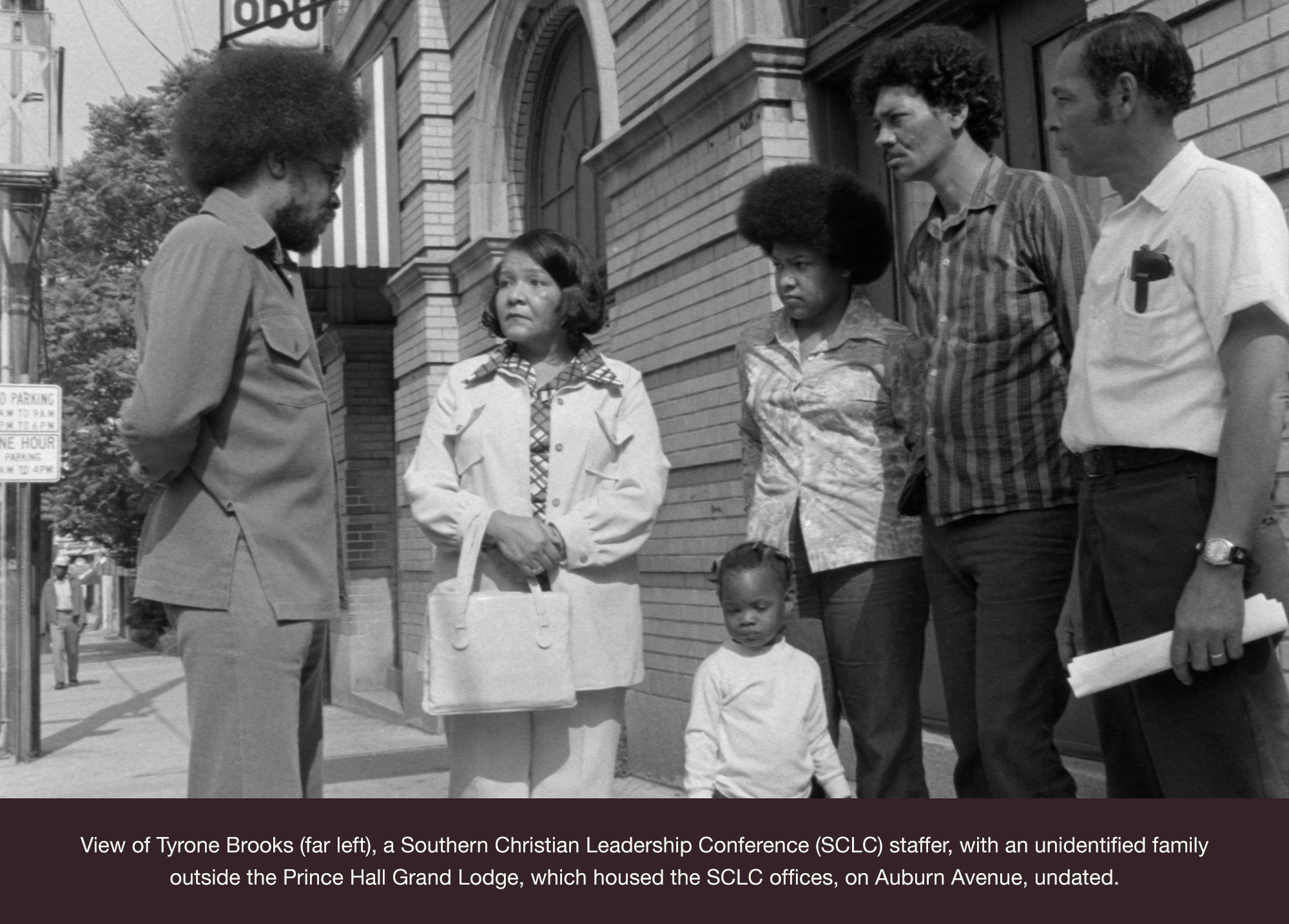 View of Tyrone Brooks (far left), a Southern Christian Leadership Conference (SCLC) staffer, with an unidentified family outside the Prince Hall Grand Lodge, which housed the SCLC offices, on Auburn Avenue, undated.