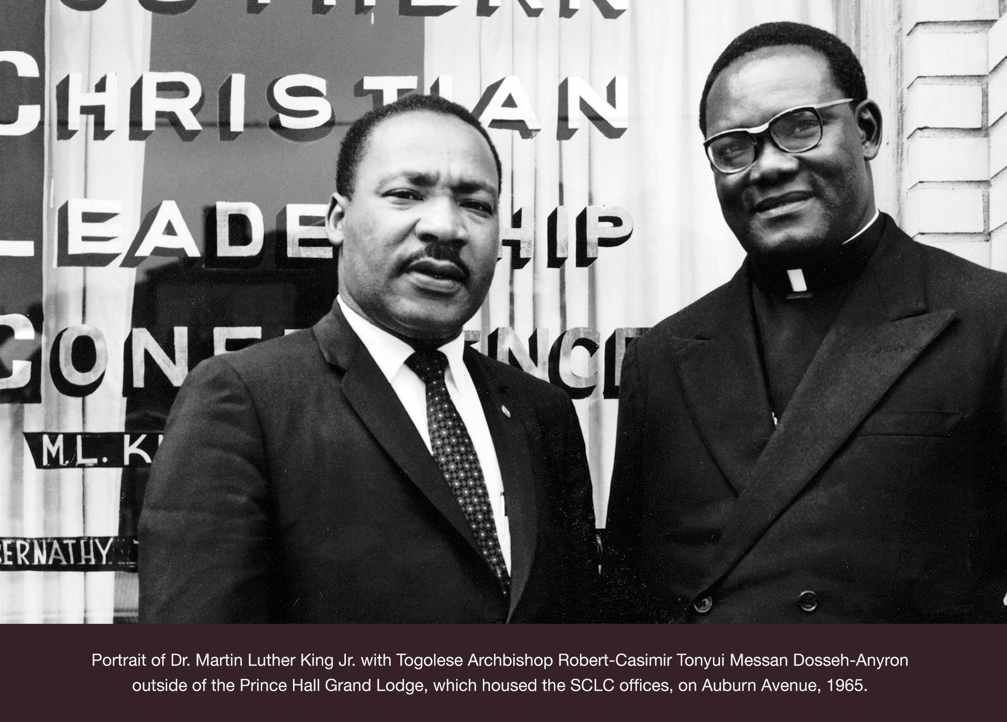 Portrait of Dr. Martin Luther King Jr. with Togolese Archbishop Robert-Casimir Tonyui Messan Dosseh-Anyron outside of the Prince Hall Grand Lodge, which housed the SCLC offices, on Auburn Avenue, 1965.
