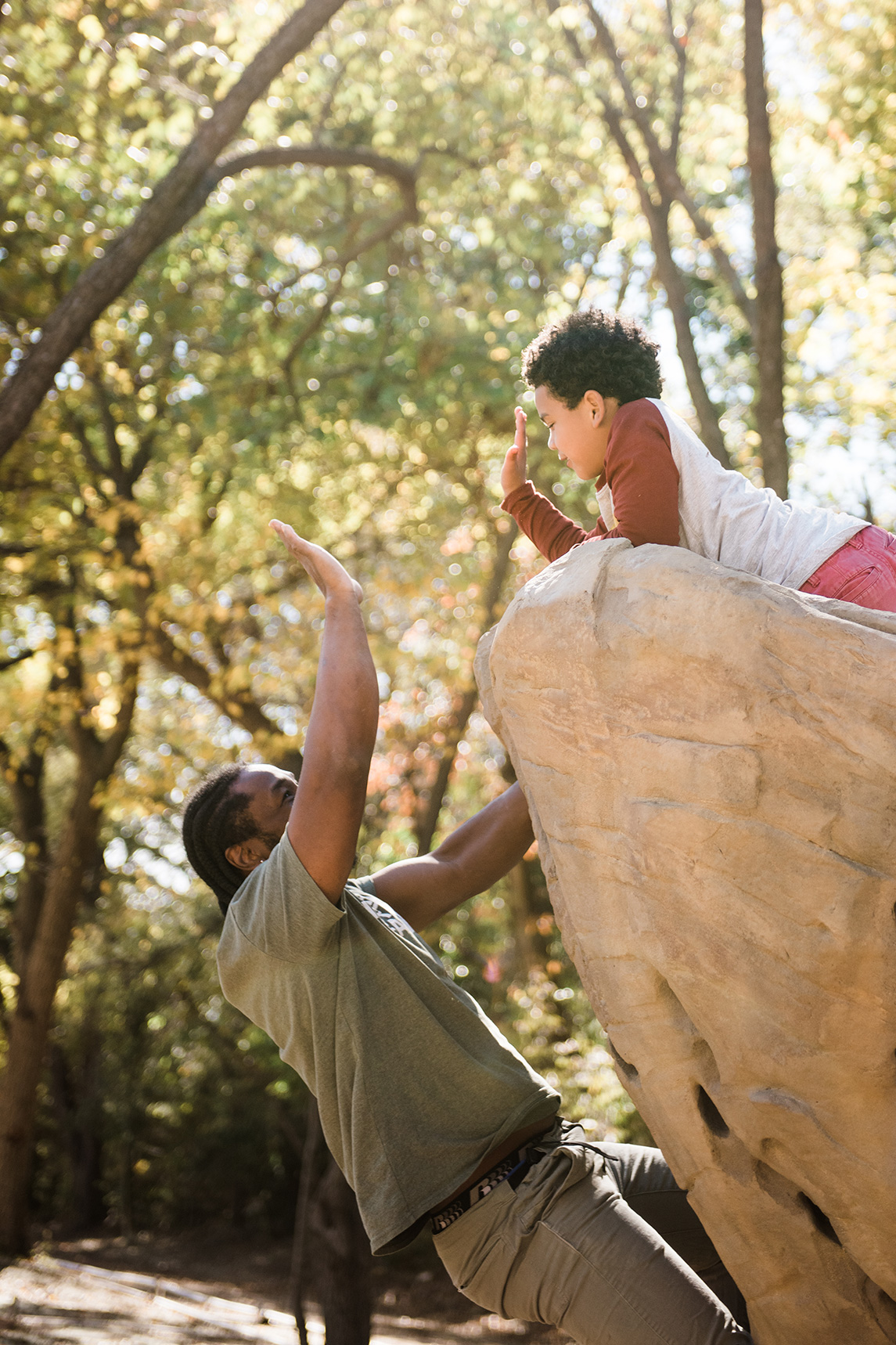 A father and son playing on a rock in a park.