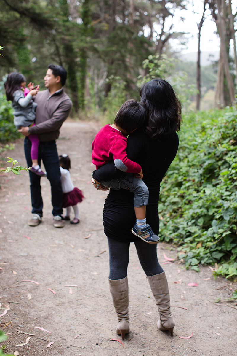 A woman carrying a child on her back in a wooded area.
